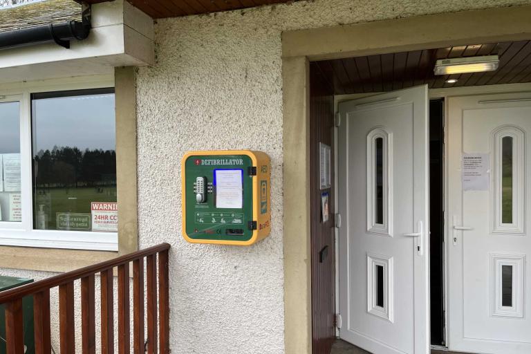 Green and yellow defibrillator mounted on dashed wall adjacent to white doors