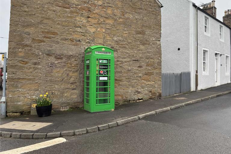 Green-painted K6 phone kiosk against a stone-built gable end of house