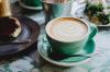 Teal cup and saucer with a latte coffee and some cakes in the background